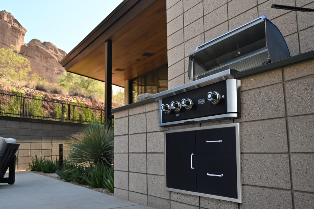 A built-in gas grill open on a stone patio island